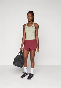 Sportinis aprangos rinkinys, sudarytas iš šviesiai žalios spalvos berankovio marškinėlio ir bordo šortų. Priedai: juoda sportinė krepšys ir juodi sportbačiai su baltais akcentais.