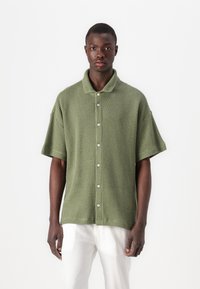Maglietta verde a maniche corte in maglia con colletto e bottoni frontali. Il tessuto strutturato ha una vestibilità morbida e un design casual.