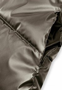 Détail d'une doudoune noire en tissu nylon glossy et lisse, avec un design matelassé et des coutures visibles le long des seams.