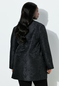 Sort stoffrakke med blomstertekstur og skræddersyet pasform. Har lange ærmer og en lige snit, der når til midt på låret.