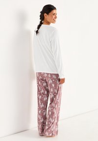 Vit långärmad topp parat med rosa mönstrade pyjamasbyxor som har vita träd och hjortar, gjorda av mjukt tyg för komfort.