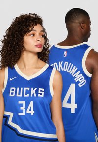 Mėlynos krepšinio marškinėliai su baltais akcentais, ant priekio esantis užrašas "BUCKS" ir numeris "34", o ant nugaros - "ANTETOKOUNMPO" ir numeris "4".
