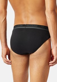 Schwarze Baumwollslips mit einem grauen "uncover"-Bund, die eine enge Passform und glatte Textur bieten, von hinten betrachtet.