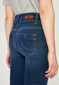 Tmavě modré džínové kalhoty s vysokým pasem, koženou značkou LTB, žlutým prošitím a zadními kapsami s nitěmi a vyšitými detaily.