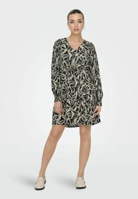 Robe à motifs floraux noir et crème avec des manches longues, un décolleté en V, une taille cintrée et une coupe décontractée. Complétée par des chaussures beiges à enfiler.