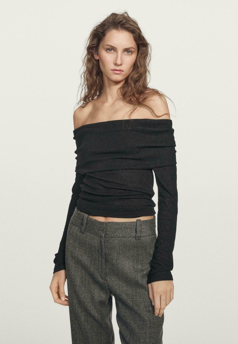 Schwarzes, schulterfreies Langarmoberteil mit strukturiertem Finish, kombiniert mit grauen, hochgeschnittenen Hosen, die über ein dezentes Karomuster verfügen.