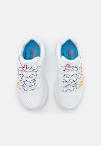 Białe buty sportowe z perforowanym cholewką, kolorowymi akcentami w pomarańczowym i różowym, oraz czarno-białymi sznurowadłami w wzory. Widoczna niebieska wkładka.