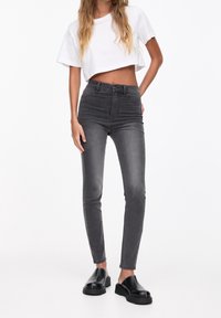 Vyötäröltä korkeat, kapealahkeiset harmaat farkut, valmistettu denim-kankaasta. Varustettu napin suljennalla ja hillityllä haalistuksella. Yhdistetty valkoiseen lyhytvartiseen t-paitaan ja mustiin jalkineisiin.