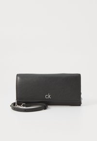 Czarny portfel ze skóry o eleganckim designie, z srebrnym logo "ck" i odpinanym paskiem na nadgarstek. Gładka faktura z minimalistycznymi akcentami.