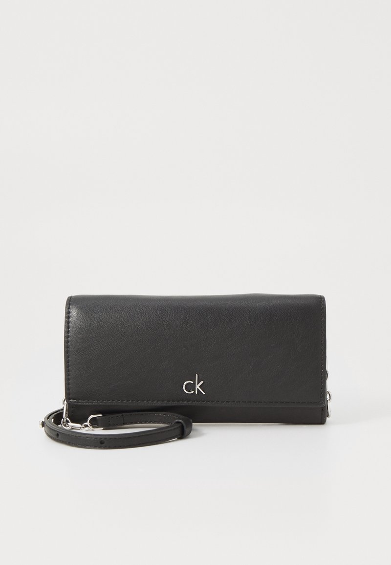 Czarny portfel ze skóry o eleganckim designie, z srebrnym logo "ck" i odpinanym paskiem na nadgarstek. Gładka faktura z minimalistycznymi akcentami.