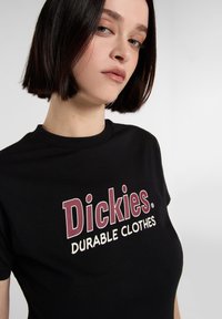 Sort bomulds T-shirt med et stort grafik i bordeaux og hvid tekst: "Dickies Durable Clothes" på forsiden, med en klassisk rund halsudskæring.