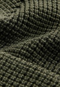 Tissu tissé vert olive, arborant un motif texturé en forme de grille. Texture douce et pelucheuse avec des fibres visibles et une surface inégale.