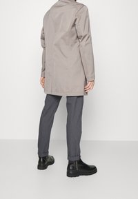 Cappotto beige chiaro di lunghezza intermedia con un design strutturato, abbinato a pantaloni grigi leggermente svasati e stivaletti neri alla caviglia con punta arrotondata.