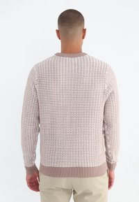 Sweter z teksturowanym splotem w kolorze beżowym z lekkim wzorem, z prążkowanym kołnierzykiem i mankietami, uzupełniający dopasowane kremowe spodnie.