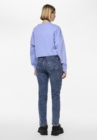 Light purple oversized sweatshirt with dropped shoulders, paired with high-waisted blue denim jeans featuring a faded texture and back pockets.