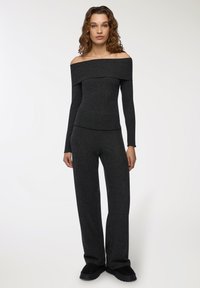 Top z dekoltem typu off-the-shoulder, prążkowany, w ciemnoszarym kolorze, z długimi rękawami, zestawiony z szerokimi spodniami w tym samym odcieniu i czarnymi butami typu slip-on.