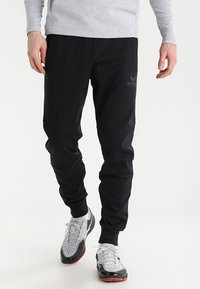 Pantalons de jogging noirs avec une coupe fuselée, fabriqués dans un tissu lisse, dotés d'une taille élastique et d'un détail de logo sur la cuisse gauche.