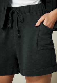 Tamno sivi šorc s rebrastom teksturom, elastičnom strukom i podesivim vezicom. Ima bočne džepove i opušteni kroj.