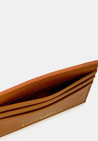 Portefeuille en cuir brun avec une finition texturée, comportant plusieurs fentes pour cartes et une doublure intérieure contrastante. Logo doré estampé sur le côté.