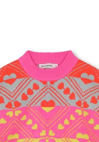 Kleurvolle gebreide trui met een geribde roze kraag, geometrische hartpatronen in oranje, grijs en geel tegen een roze achtergrond.