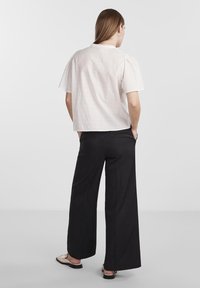 Fehér, texturált, rövid ujjú blúz, kerek gallérral, fekete, bő szárú nadrággal és lapos slip-on cipővel párosítva.