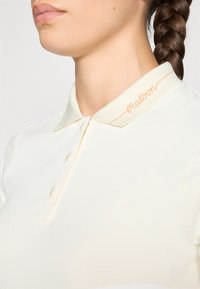 Lys beige polo skjorte med en subtil glans, som har en liten krage, oransje søm og ordet "malbon" brodert på kragen.