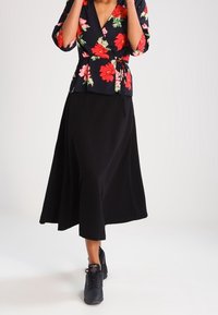 Jupe noire longueur genou associée à un haut portefeuille à fleurs sombres avec des fleurs rouges et roses. Des baskets complètent la tenue. Tissu lisse, coupe décontractée.