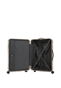 Tvrdý kabinový kufr béžové barvy se zipovým přihrádkou a černým vnitřkem. Má křížové popruhy a 360stupňová otočná kolečka.