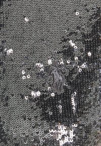 Tela de lentejuelas negra y plateada con una superficie brillante y texturada, que presenta lentejuelas redondas y superpuestas que crean un patrón reflectante.