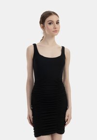 Rochie neagră, ajustată, din material cu nervuri, având bretele groase și volane orizontale de la guler până la tiv. Textură netedă și lungime deasupra genunchiului.