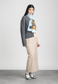 Pilka megzta džemperis, kreminių spalvų kelnės ir šviesiai mėlyna šalikas su lokio grafika. Juodi aukštakulniai ir balti kojinaitės užbaigia aprangą.