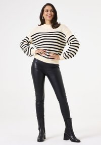 Gehaakte crèmekleurige en zwarte gestreepte trui met ballonmouwen, gecombineerd met zwarte nepleer leggings en enkellaarsjes.