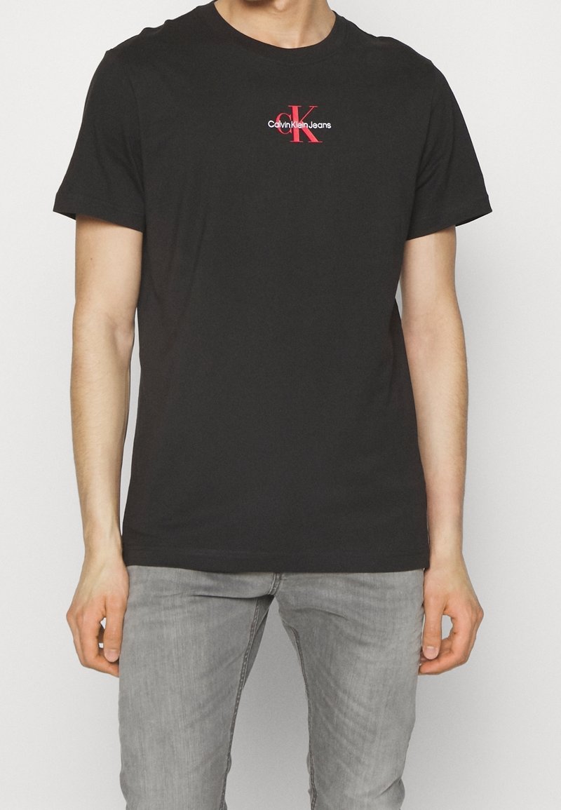 T-shirt in cotone nero con collo a giro, maniche corte e logo rosso di Calvin Klein Jeans. Il tessuto appare liscio e ha una vestibilità comoda.