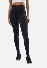 Leggings negros de cintura alta hechos de material elástico, con una textura suave y un diseño ajustado, combinados con zapatillas deportivas negras.