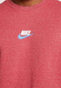 Rotes Baumwollsweatshirt mit strukturierter Oberfläche. Mit weißem "NIKE"-Logo und hellblauem Swoosh. Rundhalsausschnitt, legere Passform.