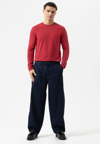 Rotes Langarmhemd, lockere dunkelblaue Jeanshose, tailliert, und schwarze glänzende Schuhe. Schlichte Gestaltung, keine sichtbaren Muster oder Verzierungen.