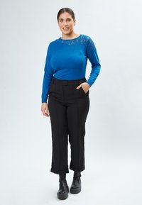 Maglione blu a maniche lunghe con dettaglio in pizzo sulla spalla, abbinato a pantaloni neri a vita alta e stivaletti neri con zeppa.