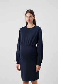 Rochie de maternitate bleumarin dintr-un material jersey moale, cu talie evazată, mâneci lungi și o lungime până la genunchi, având o textura netedă.