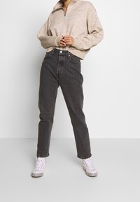 Beige vetoketjullinen collegetakki, jossa on teksturoitu kuvio, yhdistetty korkeavyötäröisiin tummanharmaisiin farkkuihin ja valkoisiin korkeavartisiin lenkkareihin, joissa on ruutukuvioiset yksityiskohdat.