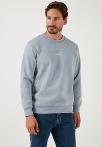 Hele hall crewneck sweatshirt ribatud kaela- ja mansettidega, millel on õrnalt tikitud bränding rindkeres. Pehme puuvilla segu kangas.