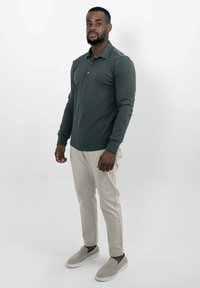 Donkergroen langemouwen polo met drie knopen, beige slim-fit broek en lichtgrijze instappers. Eenvoudig, klassiek ontwerp.