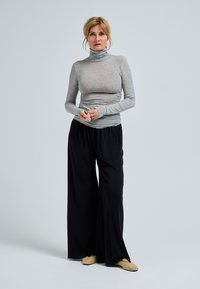 Maglione a collo alto grigio aderente con maniche lunghe abbinato a pantaloni neri larghi e morbidi. L'outfit include scarpe slip-on beige chiaro.