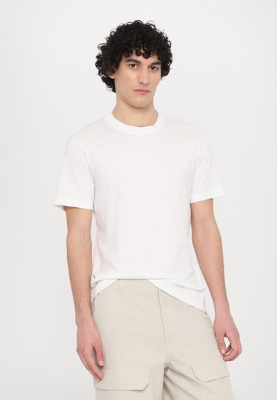 T-shirt alb din bumbac cu guler rotund și mâneci scurte, având un logo brodat discret pe piept. Textură netedă.