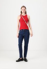 Rød ripet tanktop, blå tettsittende jeans, svarte loafers og en kremfarget skulderveske med en glatt tekstur og enkelt design.