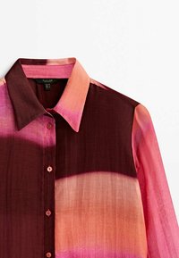 Chemise à manches longues boutonnée avec col pointu présentant des rayures horizontales en dégradé rose, pêche et bordeaux foncé.