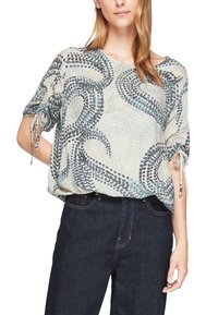 Haut léger à manches courtes de couleur crème avec un motif abstrait bleu. Présente des manches froncées et une coupe ample. Porté avec un jean foncé.