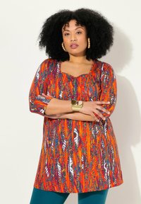 Multicolore tuniek met een abstract patroon in oranje, rood en blauw, met 3/4 mouwen en een vierkante halslijn. Draag het met turquoise broeken.