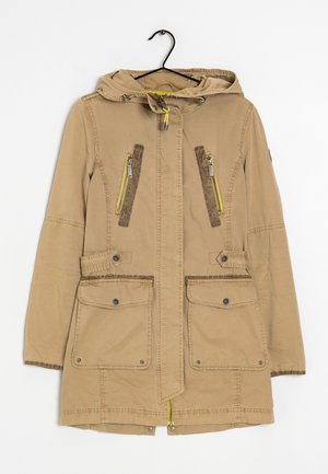 Veste à capuche marron clair avec fermeture éclair à l'avant, deux poches supérieures zippées et deux poches inférieures à rabat, suspendue à un cintre noir sur un fond blanc.