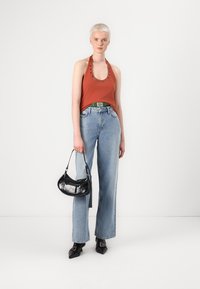 Haut halter couleur rouille avec œillets décoratifs, jean taille haute bleu clair, sac à main noir et escarpins noirs à bouts pointus.