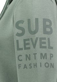 Hellgrüner Sweatshirt mit großen, fetten Schriftzug: "SUB LEVEL CNTMP FASHION." Weiche Textur mit Kapuze und gerippten Akzenten.